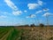 Path through a grassy fields, along a dry grass belt, overlooking distant transmitter masts and sky with clouds