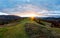 Path leading to mountain peak across meadow at sunrise