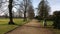 Path lined with bare trees through a park with statues and benches