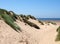 Path through tall grass covered sand dunes leading to a beach and bright blue sea in summer sunlight on the sefton coast