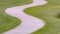 Pathway curving through grassy terrain with a pond and bench in the background