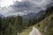 Pathway surrounded by rocky mountains covered in greenery under a stormy sky