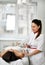 Patient is on the couch while cosmetologist starts to perform a procedure on her face with medical laser in a bright beauty shop