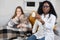 Patient and doctor. Female African doctor, visiting her sick teen girl patient at home for check up, showing to camera