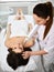 Patient lies on the couch while doctor-cosmetician performs a cosmetic procedure on her face with medical laser. In a beauty shop