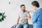 Patient sitting on couch and doctor examining patient shoulder in massage cabinet at clinic