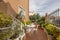 A patio of a detached house with white metal details with matching chairs and table and lots of potted plants and trees