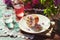 Patio table with floral cupcake, aesthetics compote and water glass. Spring lilac flowers outdoor. Creator dreamy