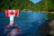 Patriot woman standing in the mazarine color water of the Cultus Lake and holding up a Canadian flag