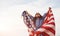 Patriotic female kid with American Flag in hands. Against cloudy sky