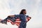 Patriotic female kid with American Flag in hands. Against cloudy sky