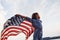 Patriotic female kid with American Flag in hands. Against cloudy sky