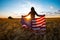 Patriotic girl with the flag of America at the wheat field against the sunset