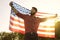 Patriotic holiday July 4th Independence Day of America. Man bearded man with the American flag in his hands at sunset in
