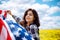 Patriotic young woman flies an american flag on a beautiful field with yellow flowers. USA independence day 4th of July