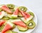 Pattern of pieces of watermelon, kiwi, lime and melting ice cubes in a plate on a gray marble background with space for
