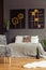 Patterned armchair next to bed in grey bedroom interior with black posters and plants.