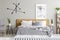 Patterned blanket on wooden bed and armchair in grey bedroom interior with poster and plants. Real photo