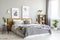 Patterned blanket on wooden bed in grey bedroom interior with plants and posters. Real photo