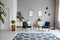 Patterned blue carpet and wooden armchairs in spacious flat interior with posters and flowers. Real photo