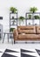 Patterned carpet in front of brown sofa next to table in white flat interior with plants. Real photo