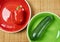 Patterned green zucchini squash on a green plate and red bell pepper on a red plate next on a cane place mat