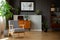 Patterned wooden armchair next to plant in grey living room interior with poster. Real photo