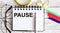 PAUSE written in a notebook on white background with office tools