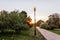 Paved path with lanterns in the city park at sunset. No people walking along the alley in the nature park