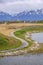 Paved pathway curving along the rocky and grassy lake shore under cloudy sky