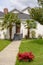 Paved pathway to the house entrance over front yard decorated with red flowers