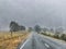 Paved road running near autumn coloured paddocks in a rainy day