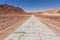 Paved road runs through Arava desert among red mountains in Timna National Park, Israel