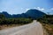 Paved rural road winding through cultivated lands having a forested mountain range in front