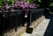 Paved sidewalk with gutter and gray metal ornate railings. lamp with glazed lampshade and black post, zig zag jagged partitions bl