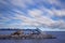 Pavement construction in middle of sea during day with long exposed clouds in background.