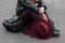 On the pavement sits a young woman in a black stylish jacket in purple pants in fashionable boots with a leather backpack