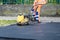 Paving worker uses vibratory plate compactor to compact new asphalt near curbstones
