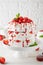 Pavlova layered cake with fresh strawberries, sauce and whipped cream on a white wooden background. Summer beautiful cake.