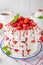 Pavlova layered cake with fresh strawberries, sauce and whipped cream on a white wooden background. Summer beautiful cake.