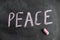 Peace. A word is written in pink chalk on a black chalkboard. Handwritten text. A piece of colored chalk hangs next to it