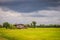 A peaceful cottage on green rice farm with dark stormy sky background. Tranquilly green rice field and farmer hut under calm sky