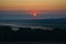 Peaceful dawn sky reveals a picturesque landscape of rolling hills dotted with trees.