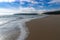 Peaceful empty golden sand beach with waves rolling in and pine forest and a large sand dune in the background