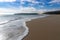 Peaceful empty golden sand beach with waves rolling in and pine forest and a large sand dune in the background