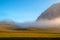 Peaceful foggy landscape with hill above the meadow of horizontal lines under the blue sky