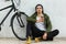 Peaceful hipster guy sits on floor outside over white background, holds papercup of hot coffee, having break. Dark haired model