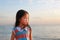 Peaceful little child girl standing on beach at sunset light with looking out