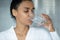 Peaceful mixed race woman in bathrobe drinking good quality water
