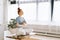 Peaceful redhead young woman female sitting in lotus pose at the desk with closed eyes